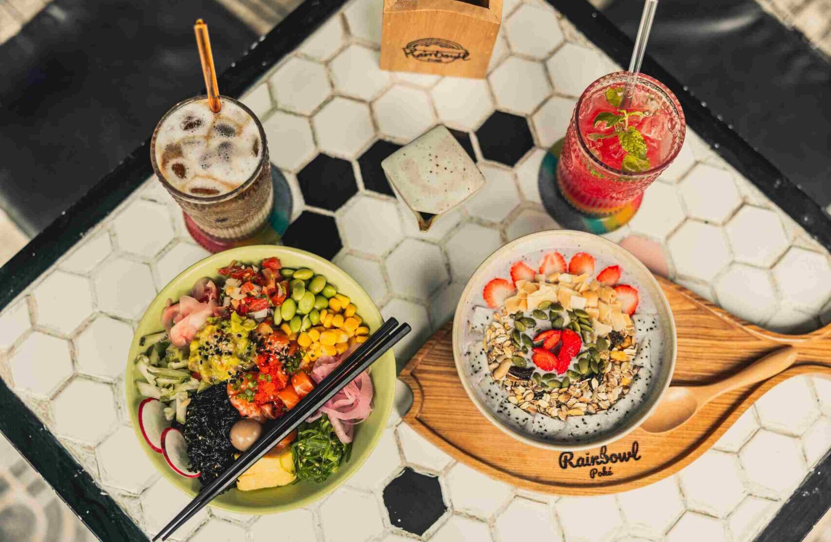 A table filled with Rainbowl Poke Food, including one Poke Bowl one Smoothie Bowl and two juices